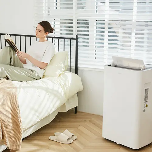Frau liest im Bett sitzend während die mobile Klimaanlage kühlt als Beispiel-Bild für die Blog-Ktegorie Raumklima
