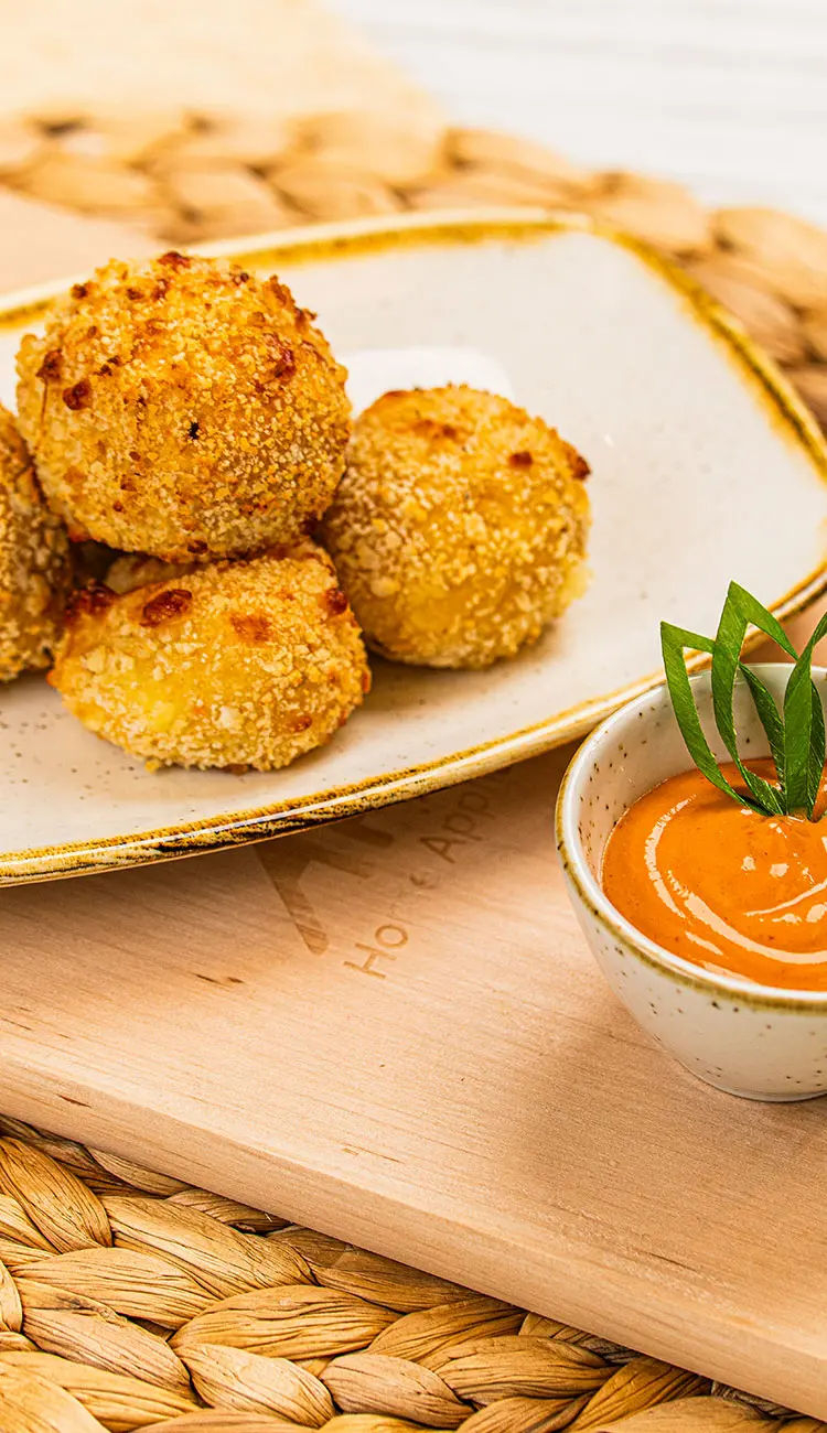 Kartoffel-Käse-Häppchen auf Teller neben Schüssel mit orangefarbenem Dipp auf einem Holzbrett als Beispielbild für die Midea Rezepte Kategorie