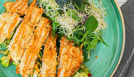 Knusprig paniertes Hähnchenfilet serviert auf einem frischen Salat 